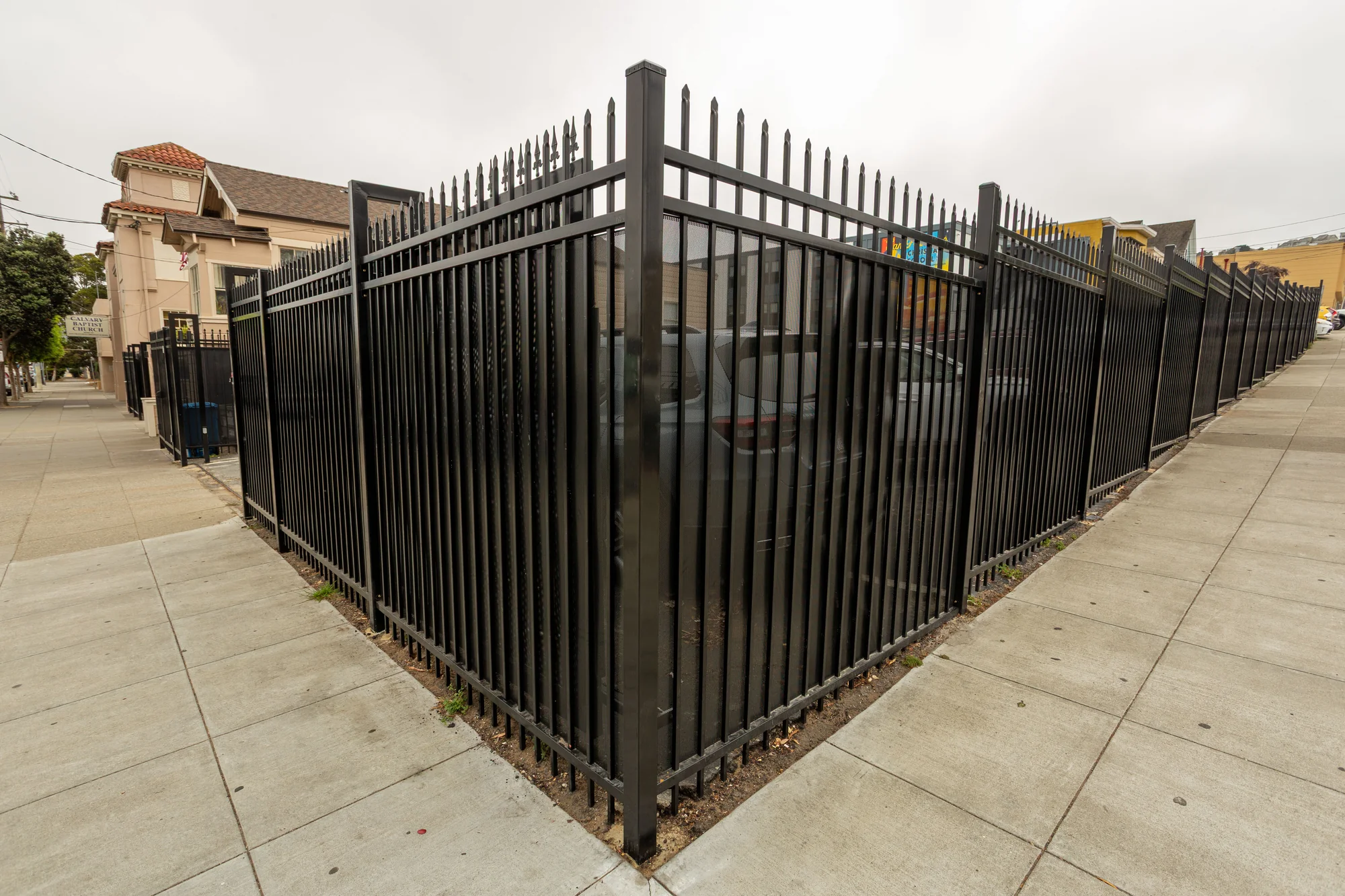 New black metal fencing wraps around the sidewalk corner beside the campus