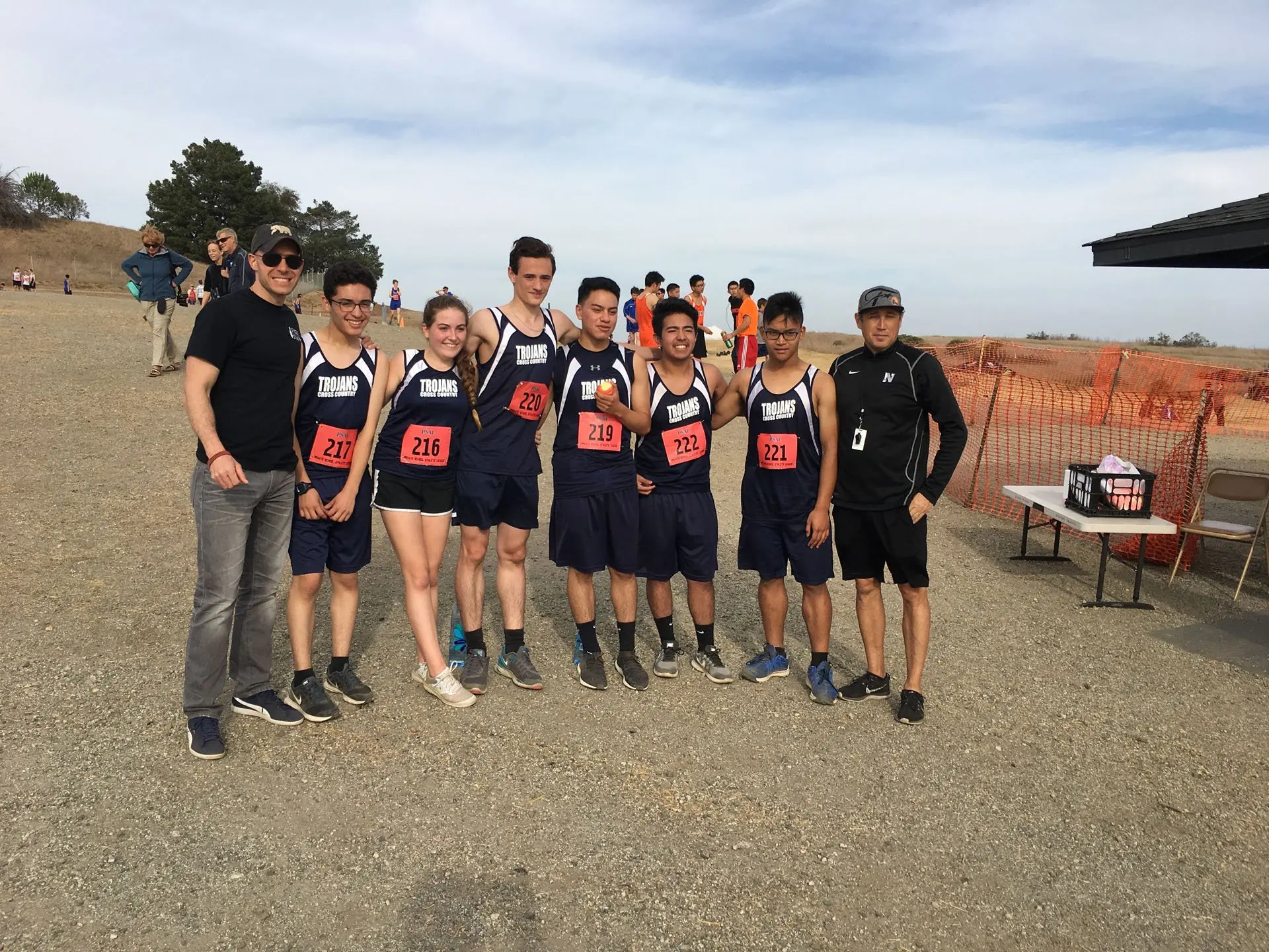 The Trojans cross country team lined up arm in arm at a meet, numbered race bibs on their singlets