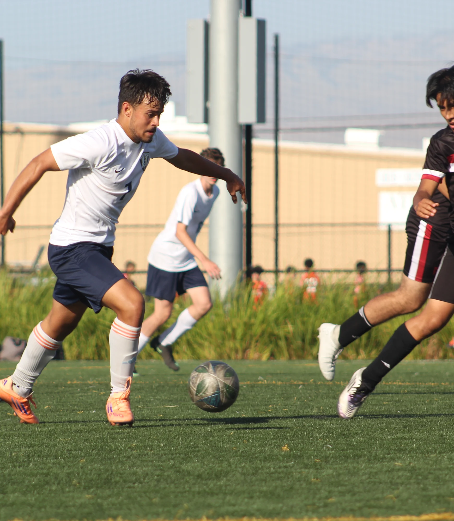 A soccer player in white dribbles the ball past a defender in black on a sunny field