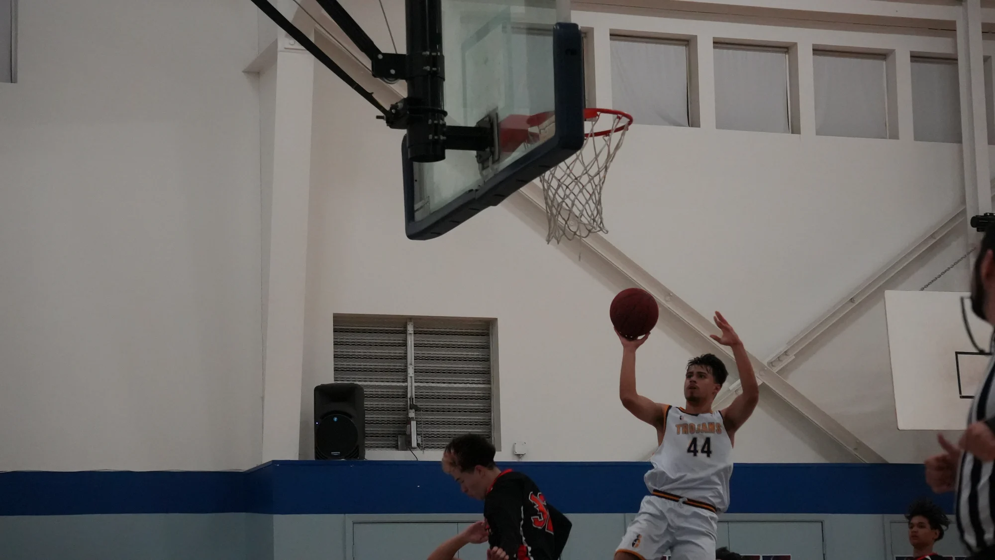 A Trojans basketball player lifting the ball toward the basket in a white jersey