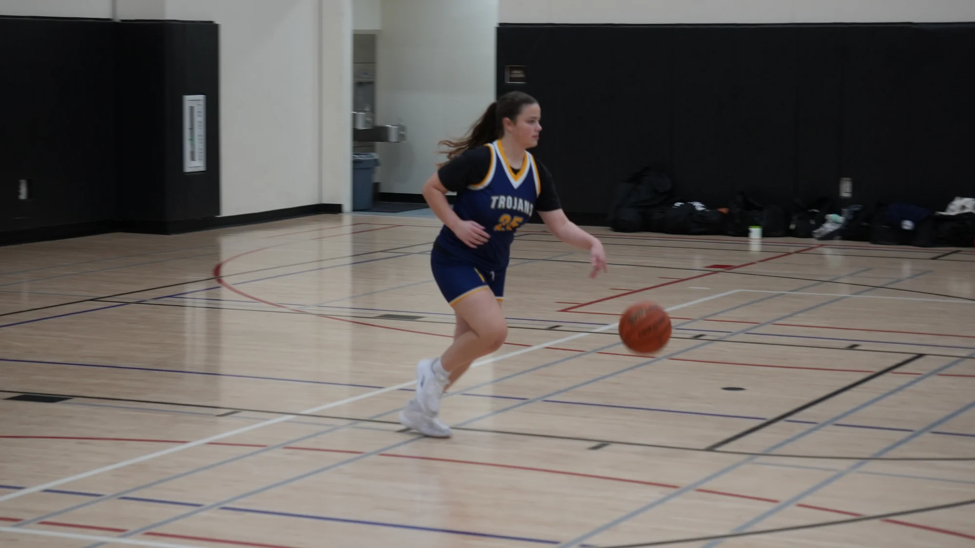 A Trojans basketball player dribbling upcourt in a navy uniform