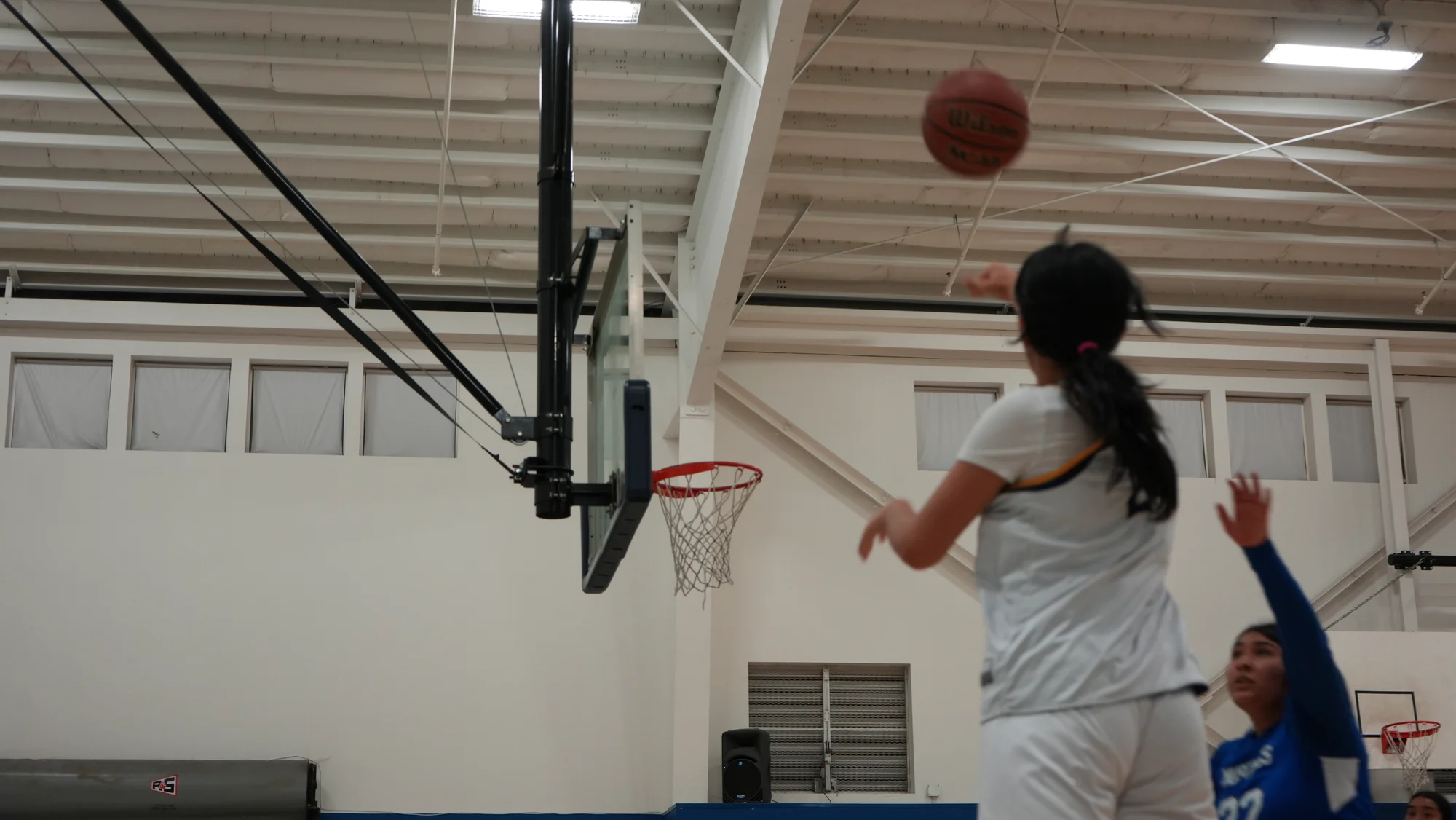 A Trojans basketball player releasing a shot toward the hoop as a defender reaches up