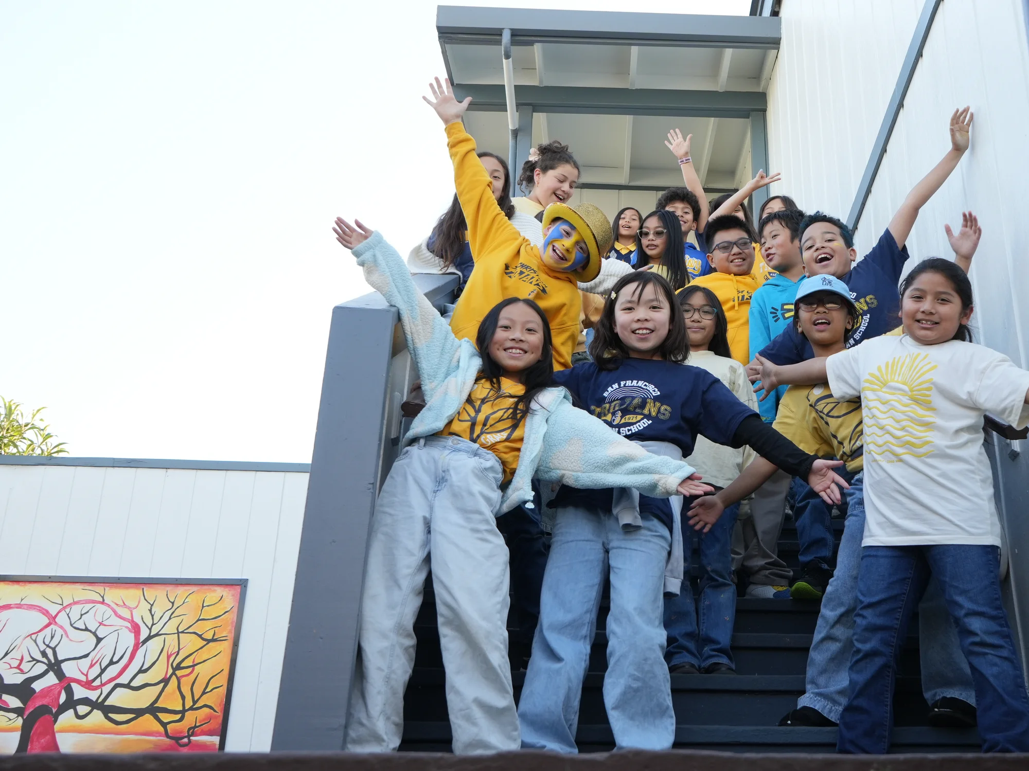 Students in blue and gold cheering with arms spread wide down the school staircase