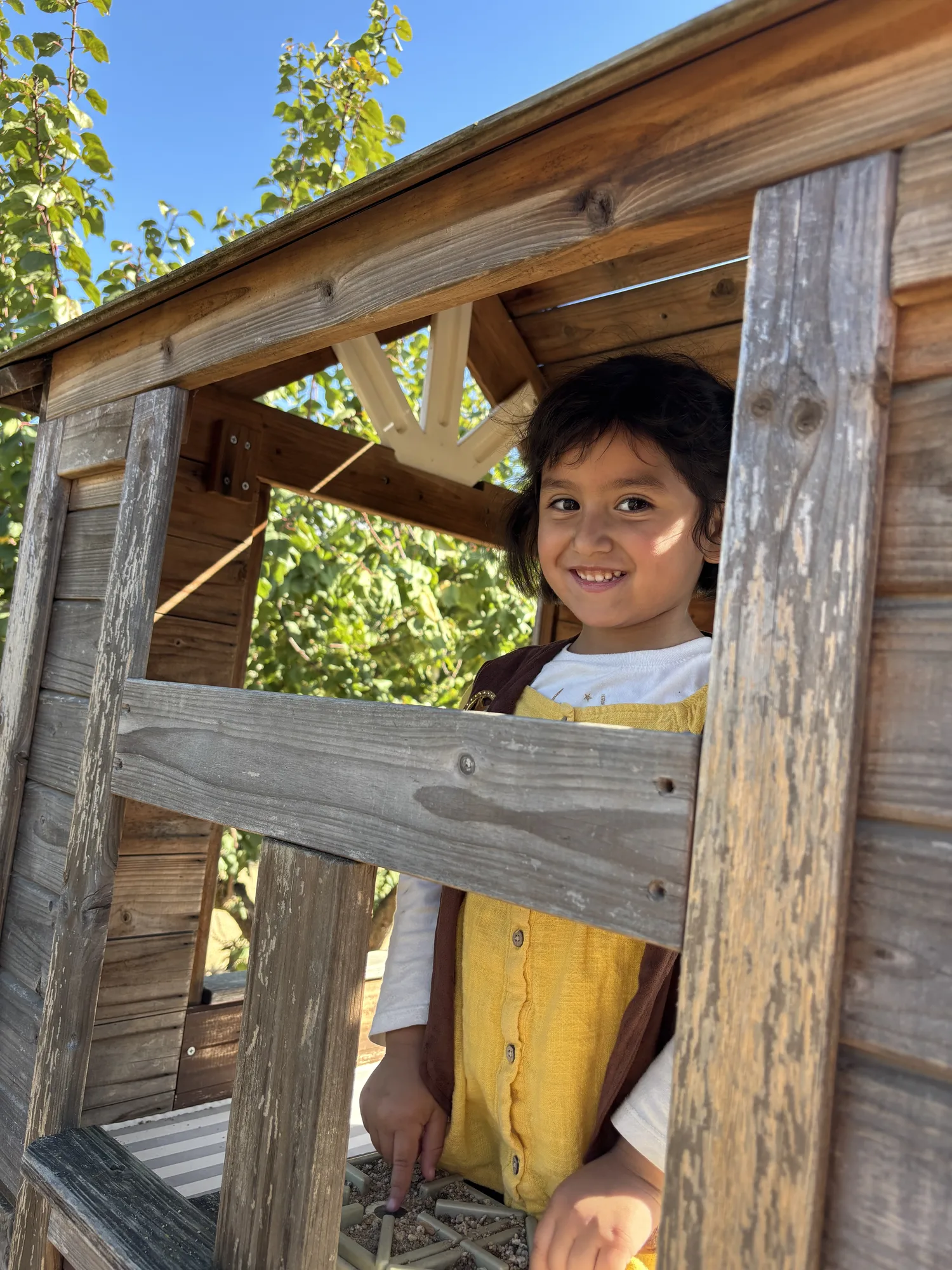 A student beaming out of a wooden playhouse window at a farm