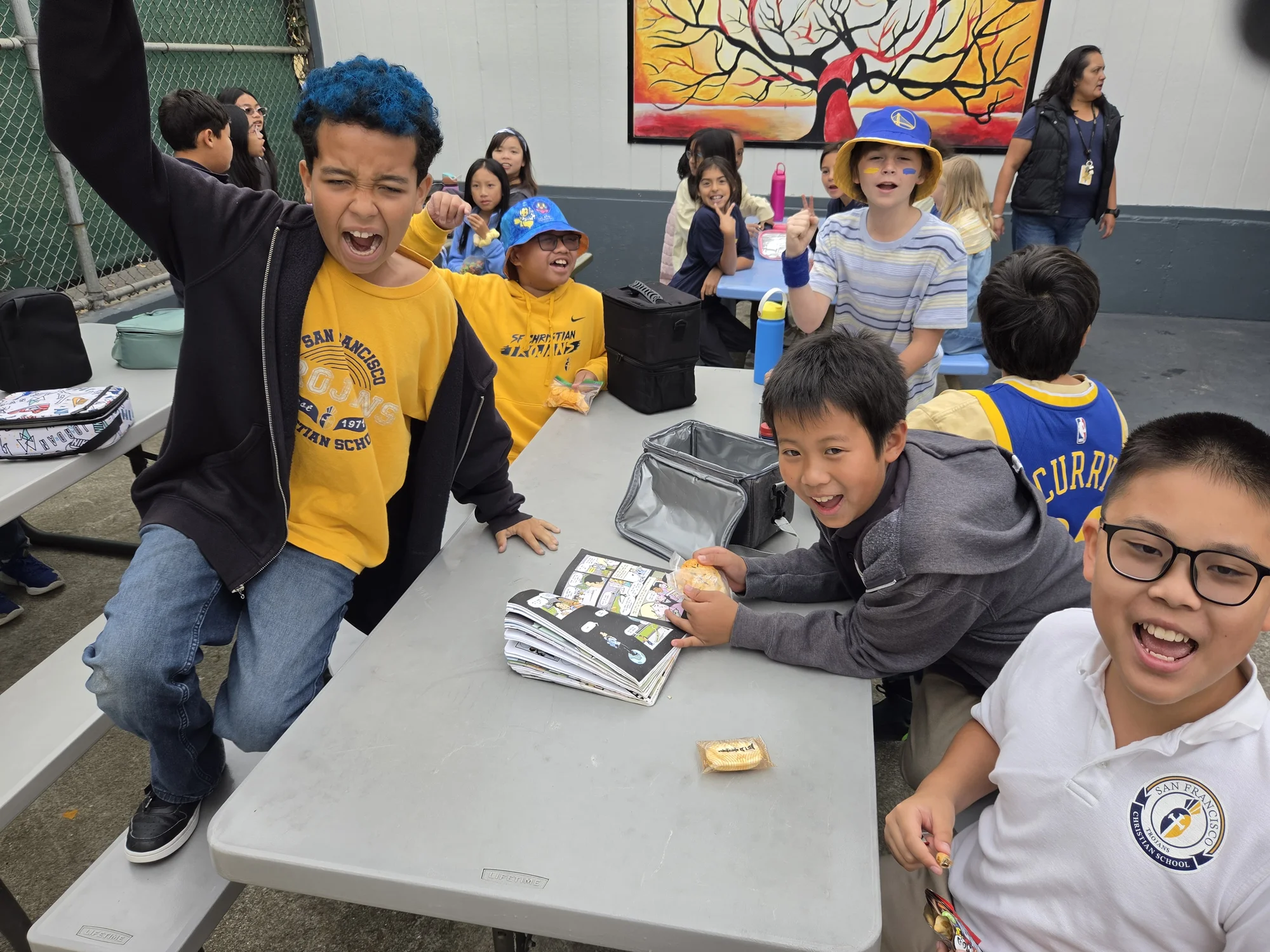 Fifth graders cheering and laughing around a lunch table outdoors