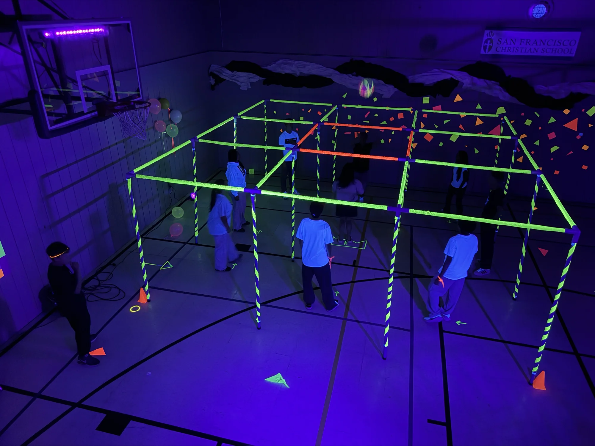 Students playing a game inside a grid of glowing frames in the darkened gym at Glow Night