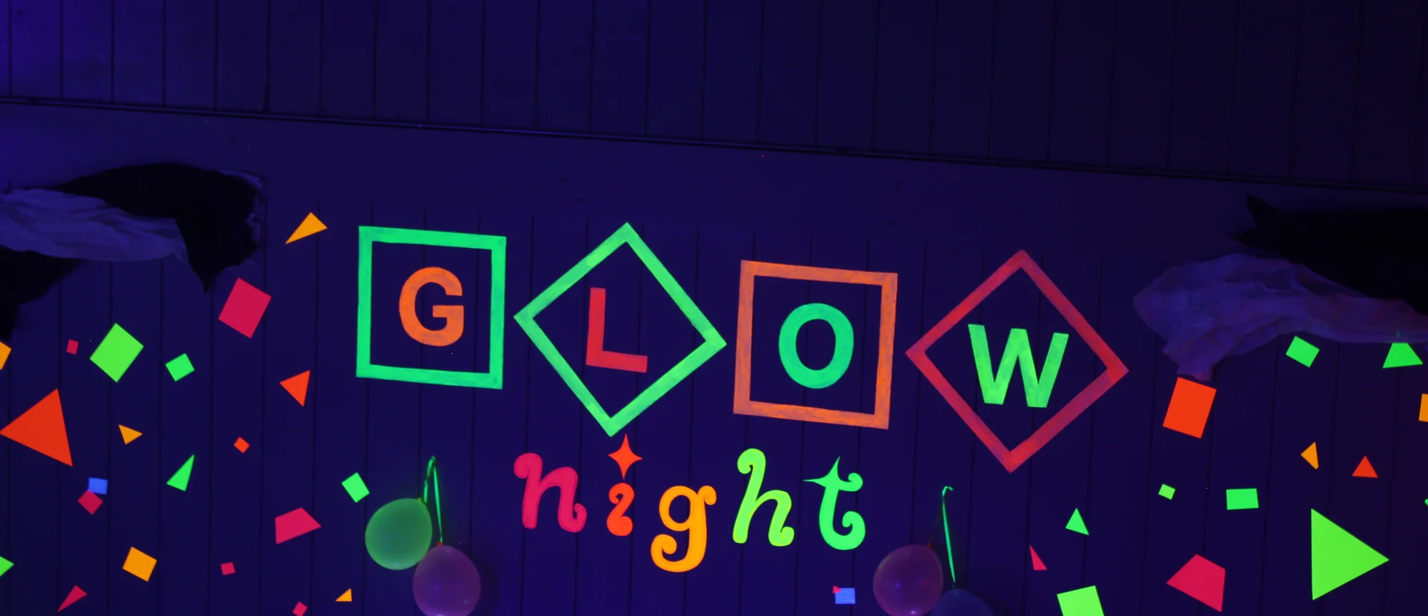 The Glow Night sign in bright fluorescent letters on the darkened gym wall