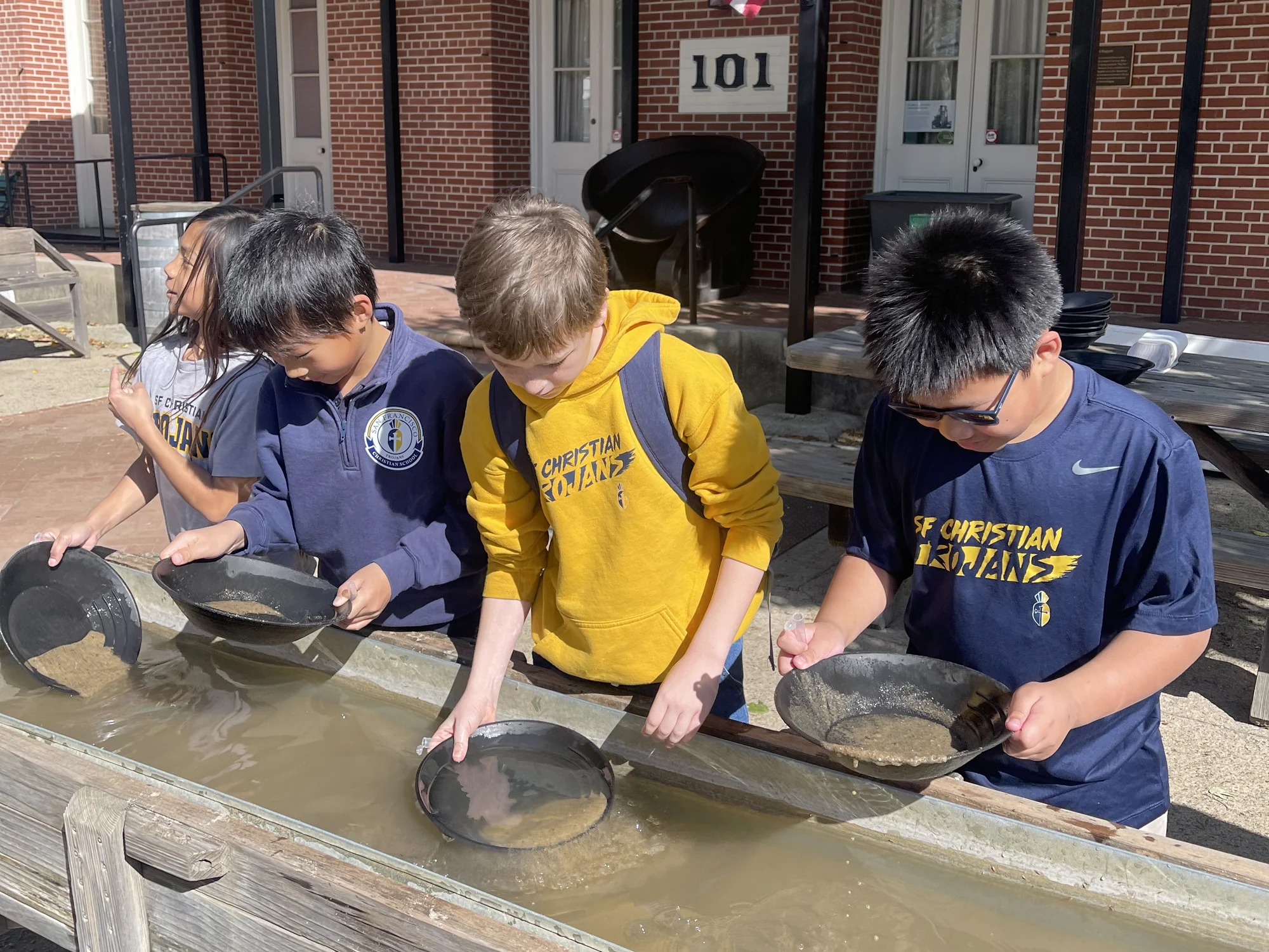 Four students panning for gold at a long water trough on a Gold Rush field trip