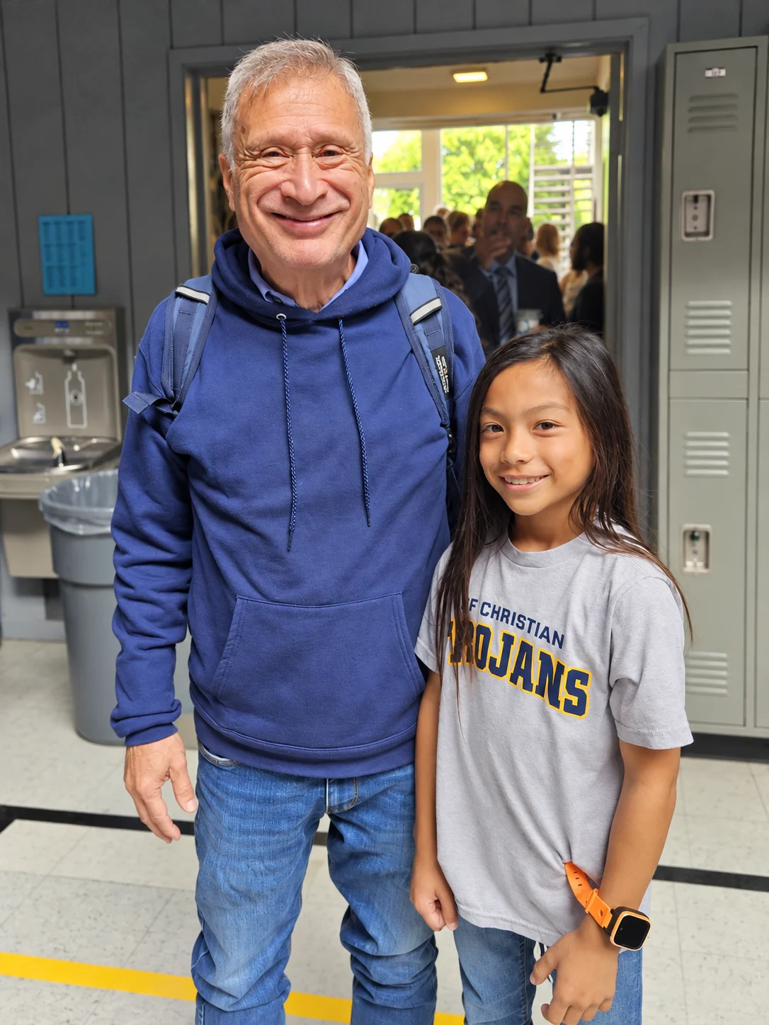 A grandparent in a blue hoodie and a student in a Trojans shirt smiling side by side