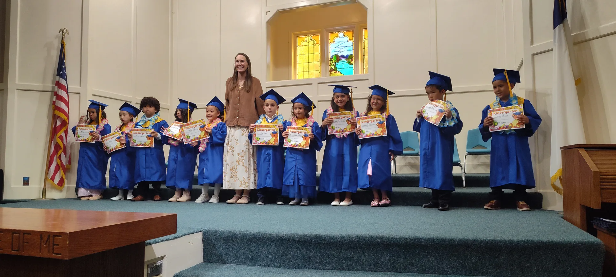 Kindergartners in caps and gowns with their teacher at graduation
