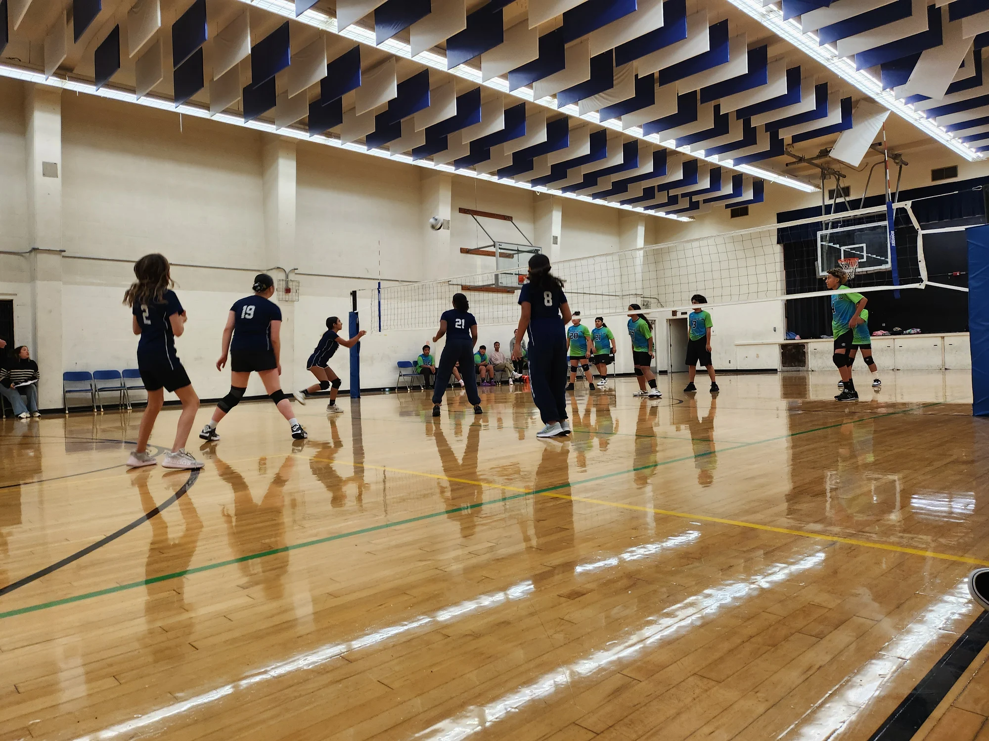 Middle school volleyball players spread across the court during a rally