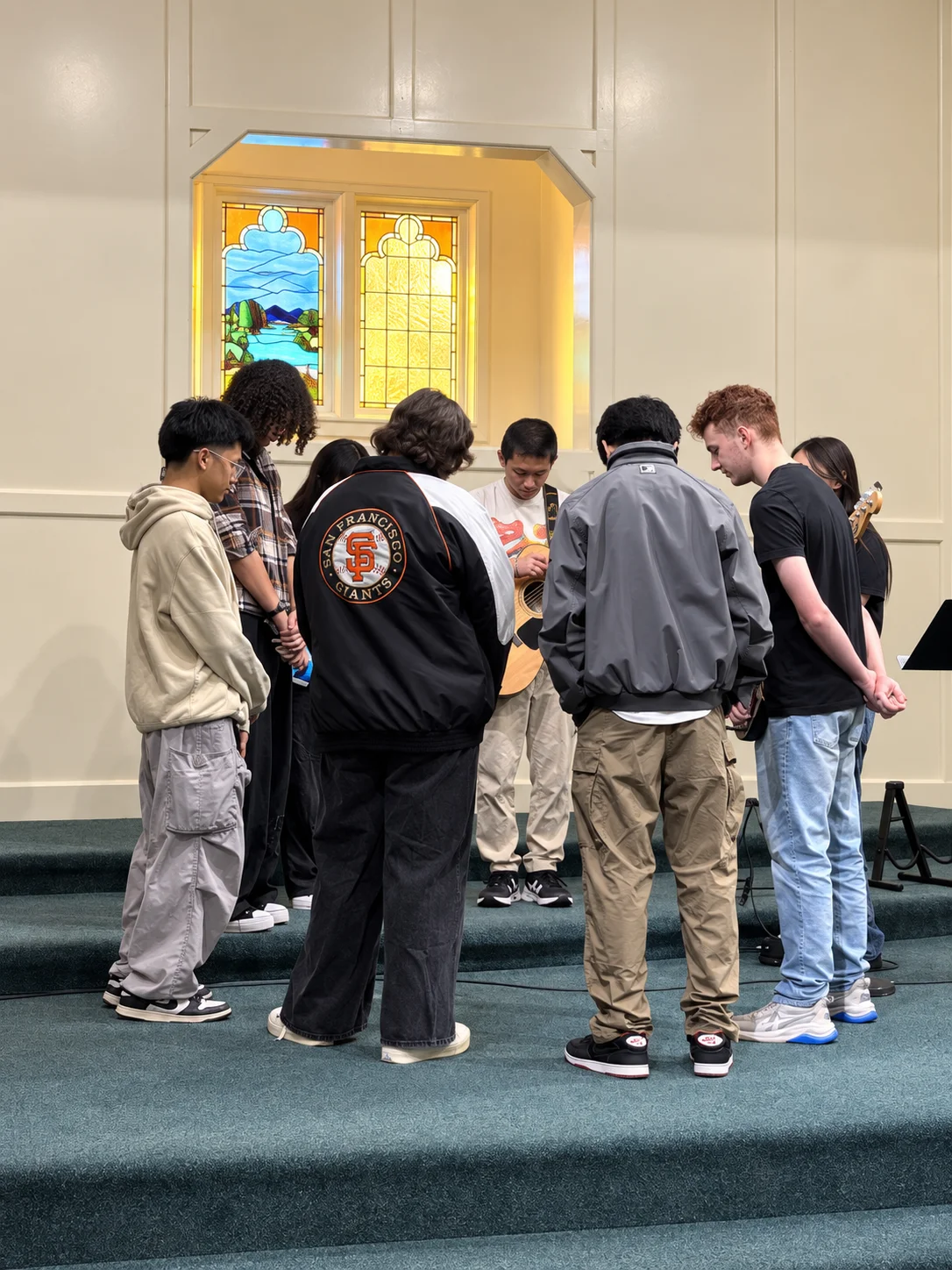 High school students standing in a circle with heads bowed in prayer before leading worship