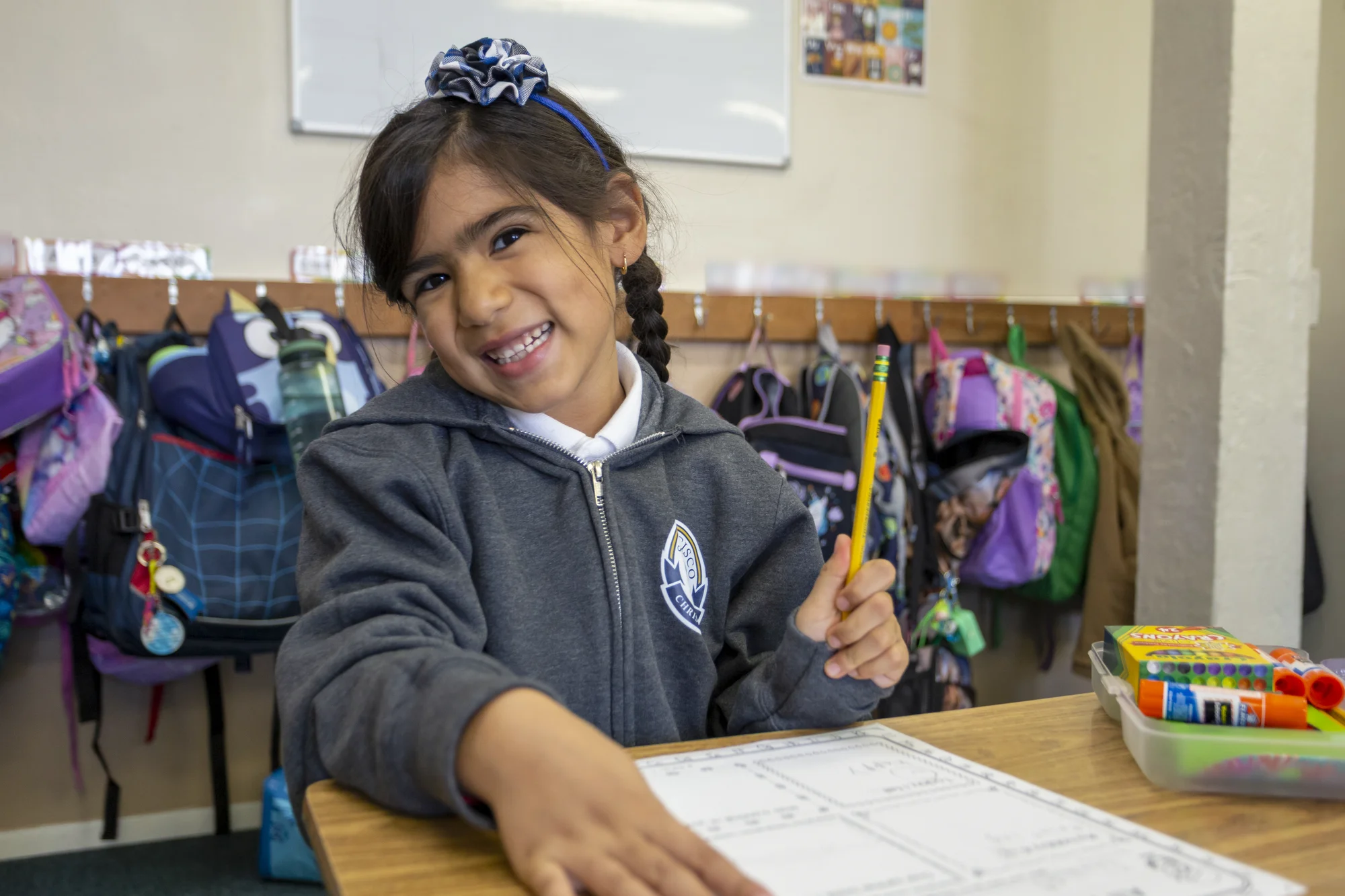 A young student smiling at her desk with pencil in hand and workbook open