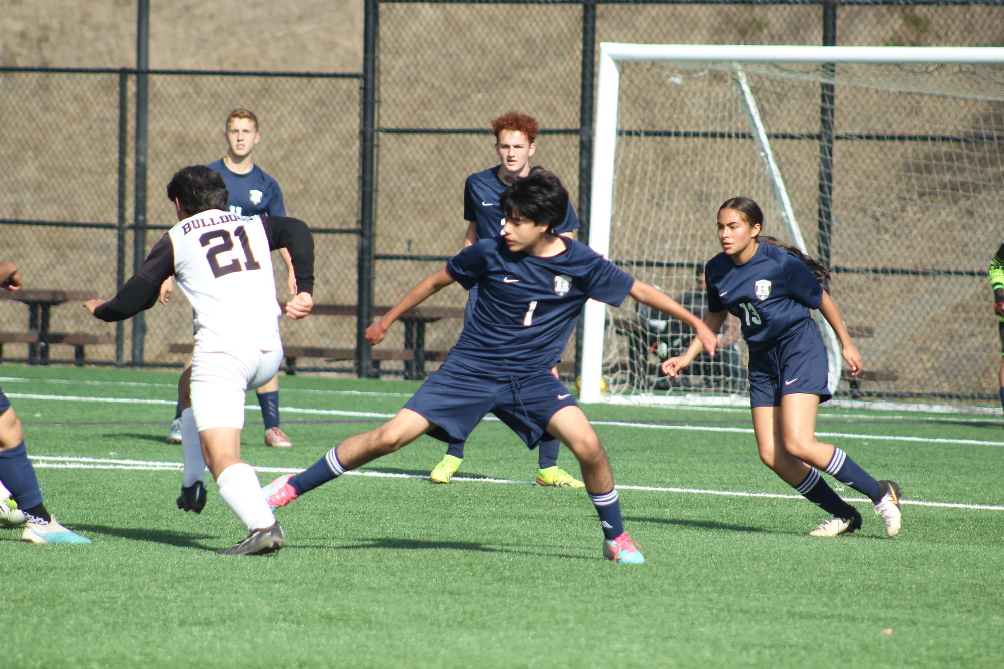 A Trojans soccer player stretching a leg to reach the ball between two opponents