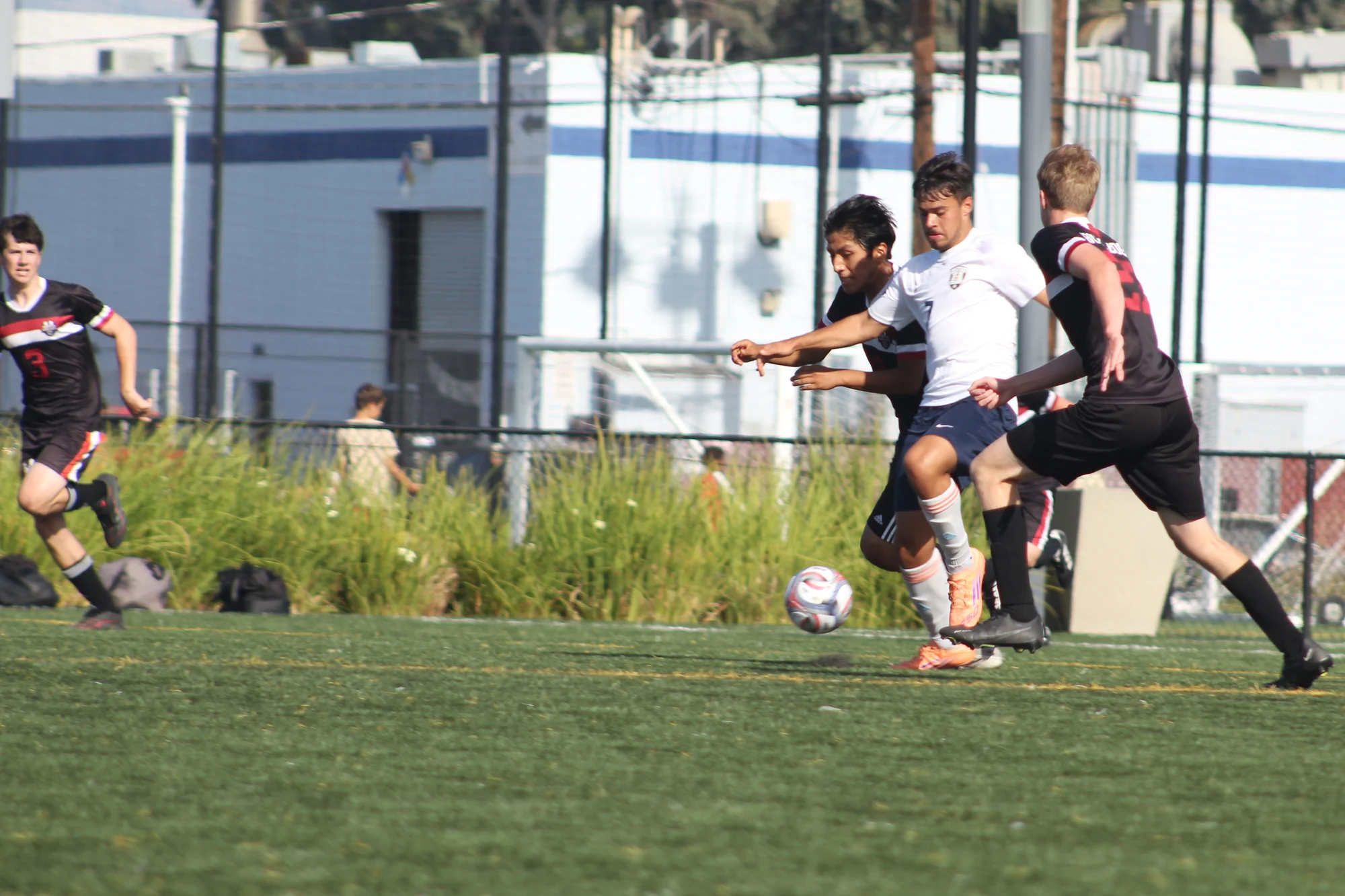 A Trojans soccer player in white battling two opponents for the ball