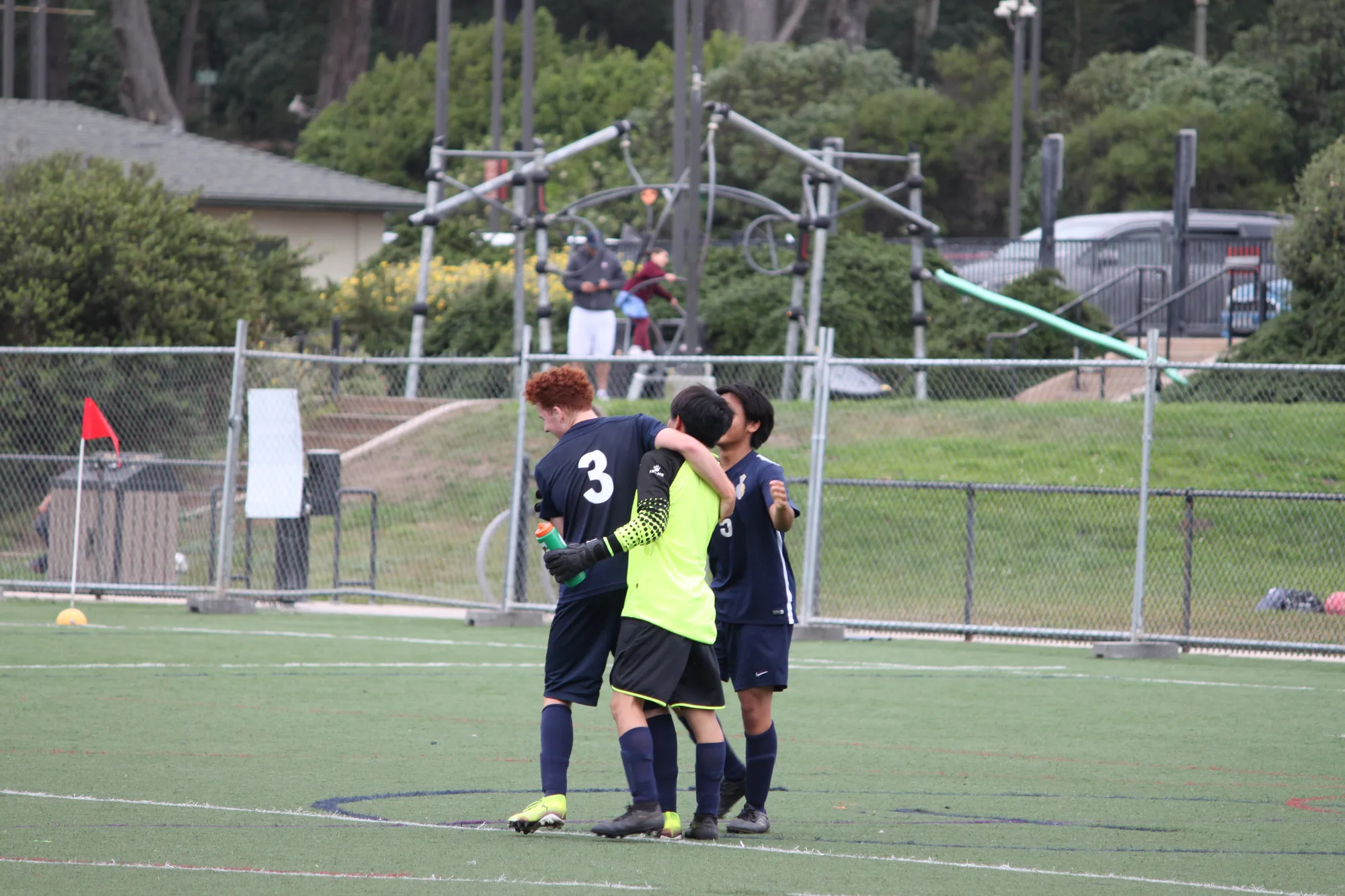 The goalkeeper kneeling with arms out in joy as teammates converge