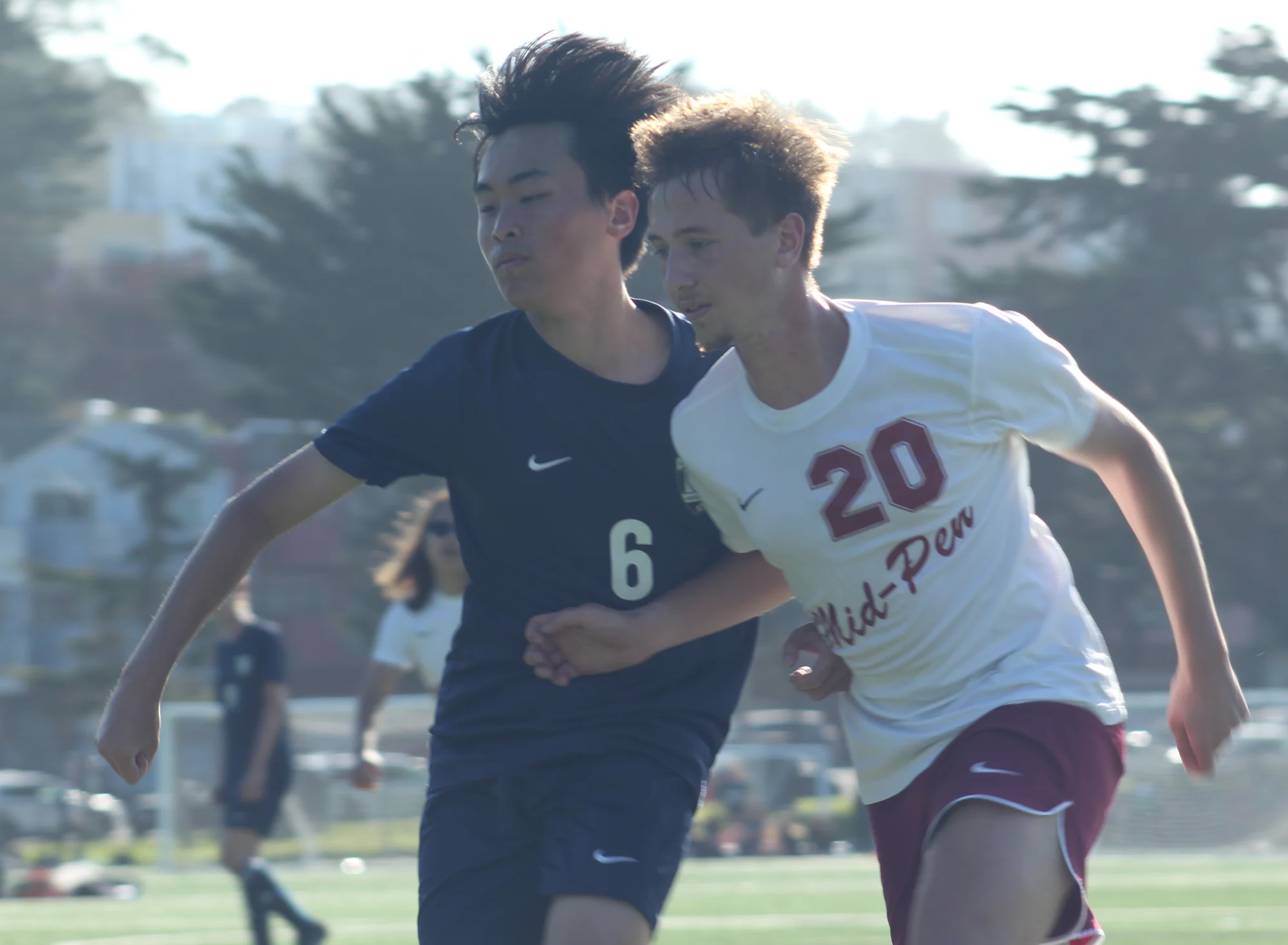 A Trojans soccer player in navy running shoulder to shoulder with an opposing player