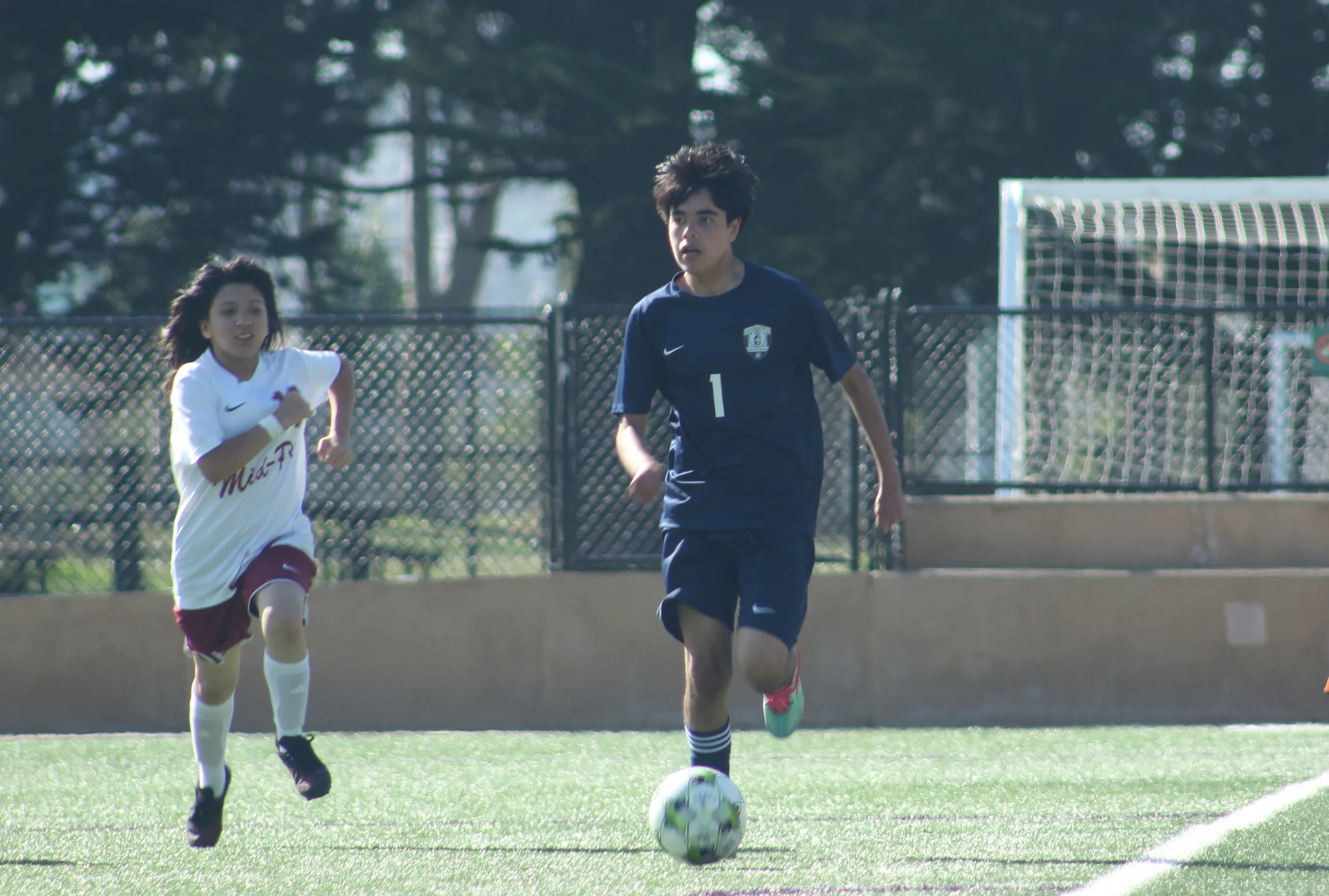 A Trojans soccer player bringing the ball up the sideline with an opponent chasing