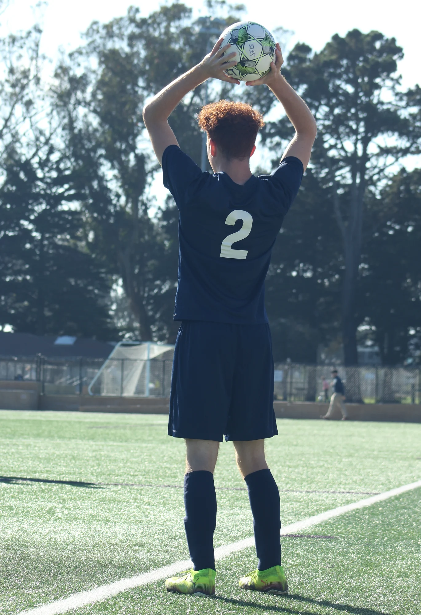 A Trojans soccer player lifting the ball overhead for a throw-in at the touchline