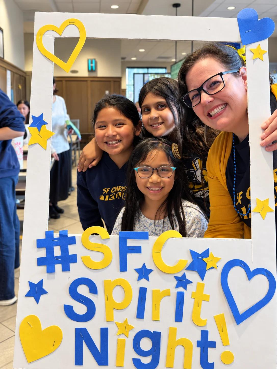 Students and a smiling adult posing inside the handmade SFC Spirit Night photo frame
