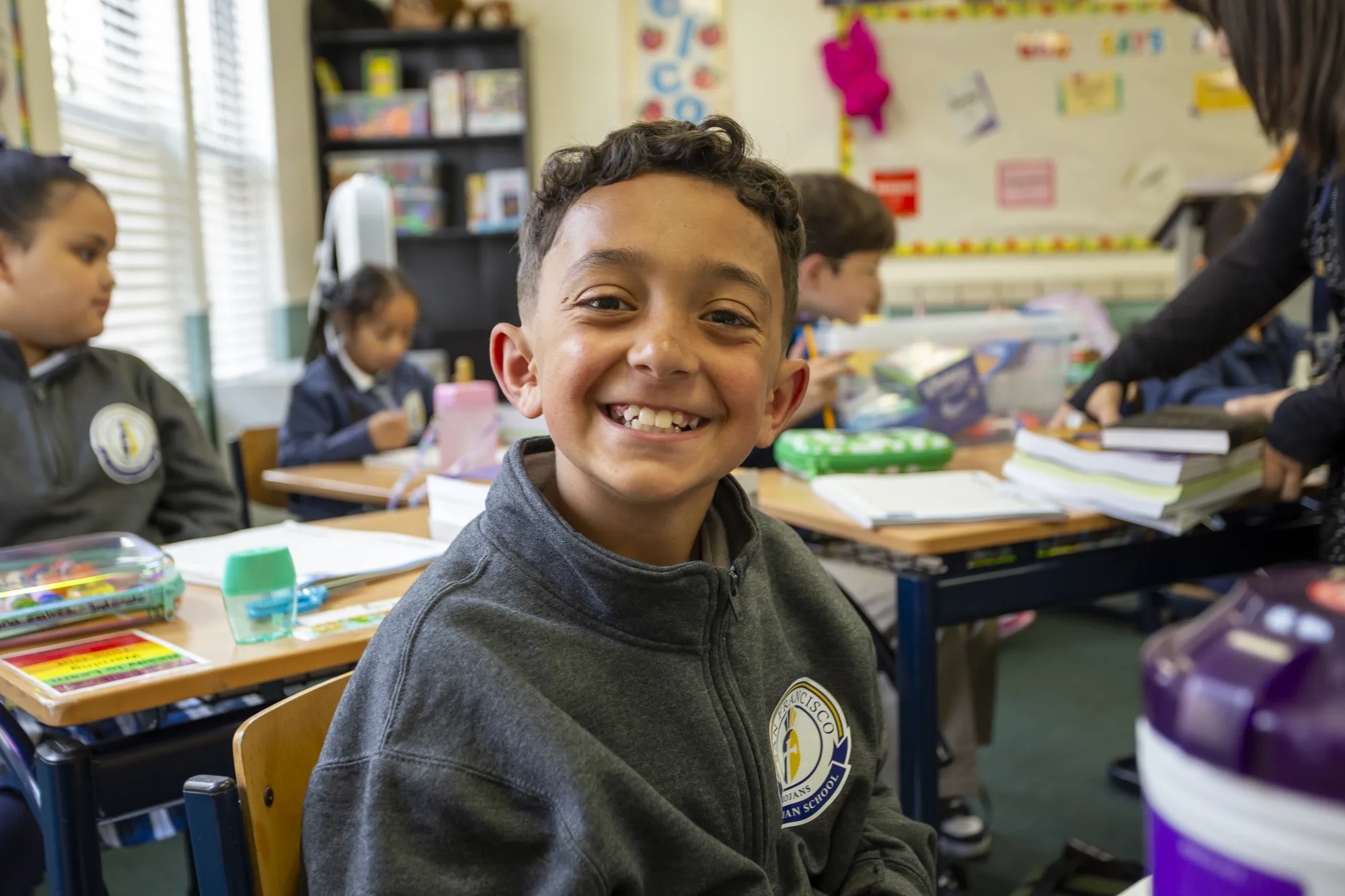 A third grader with a genuine grin in a navy school quarter-zip in the classroom
