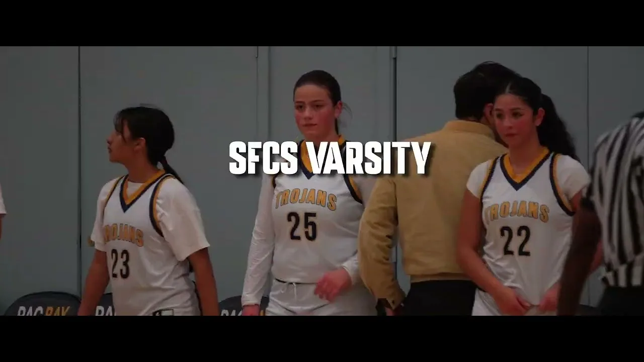 Trojans varsity basketball players in white and gold uniforms crossing the court