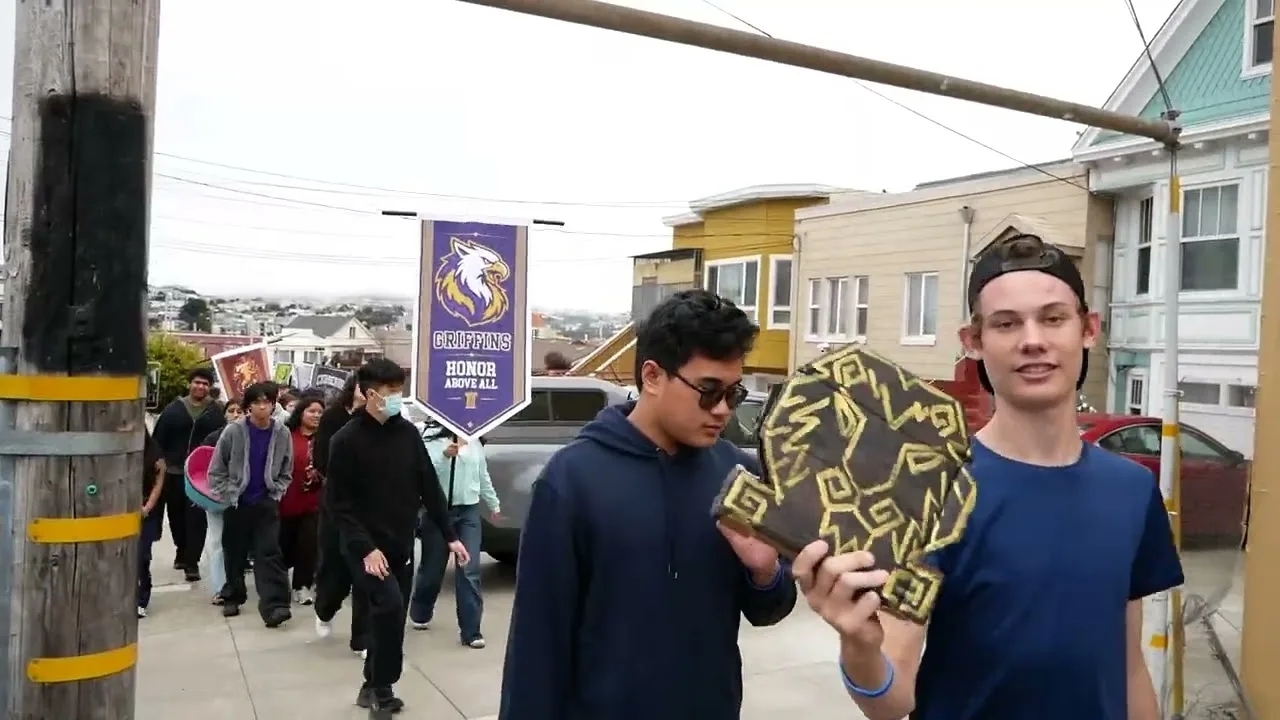 High school students carrying a team banner and a painted shield along the sidewalk