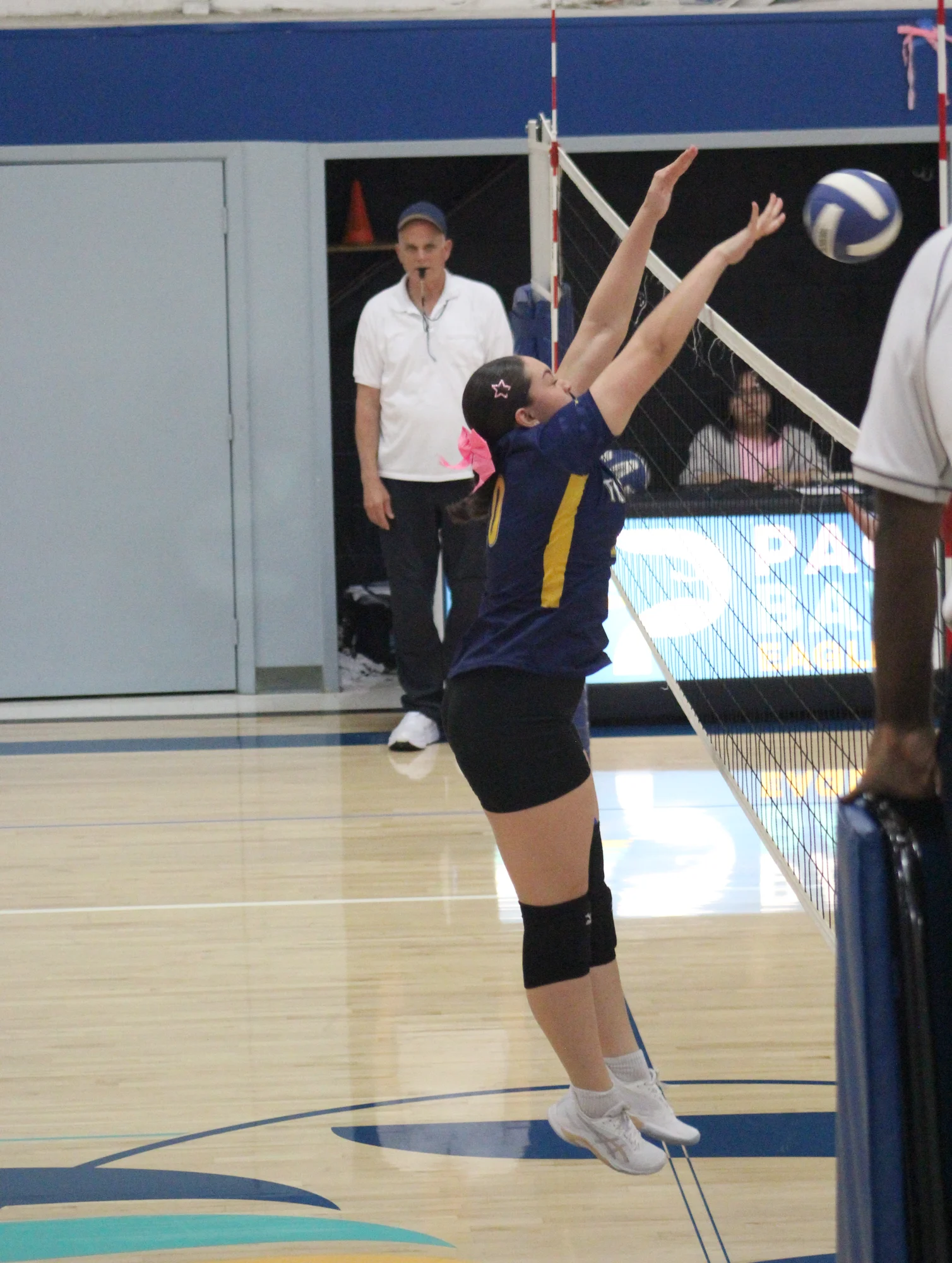 A Trojans volleyball player stretching up to set the ball beside the net