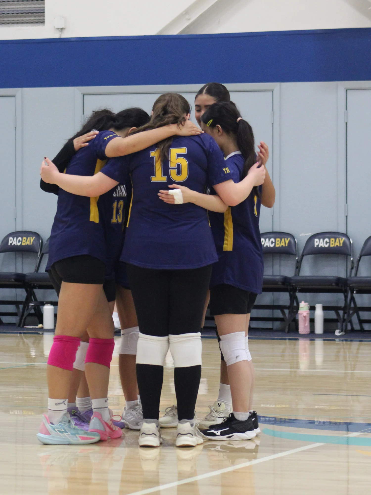 Trojans volleyball teammates standing close together with their arms around one another
